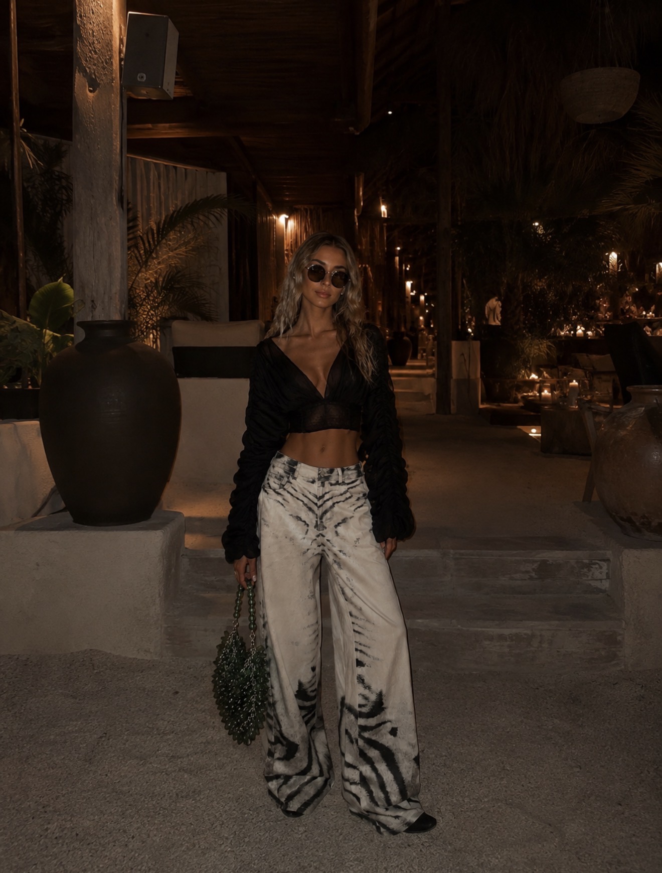 Black frilly V neck long sleeve top, zebra patterned baggy jeans, and a green bag, made out of green jewels.